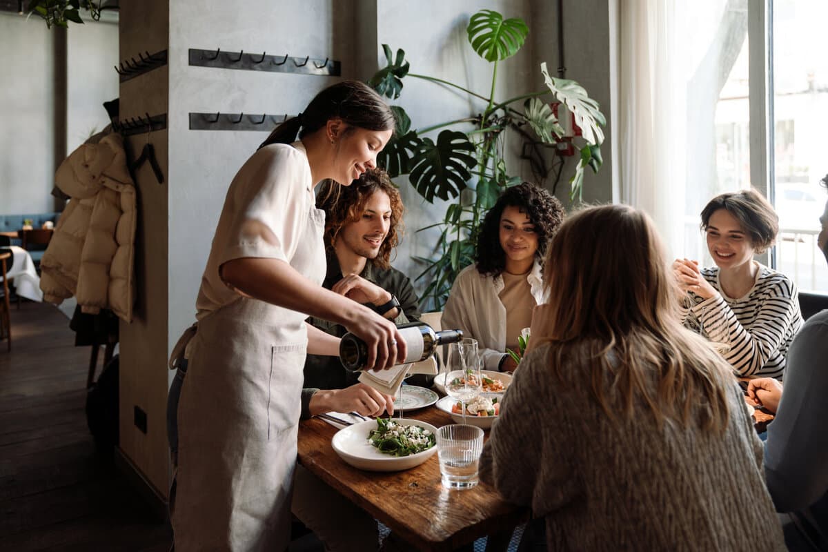A server pours wine for a table of guests in a busy restaurant